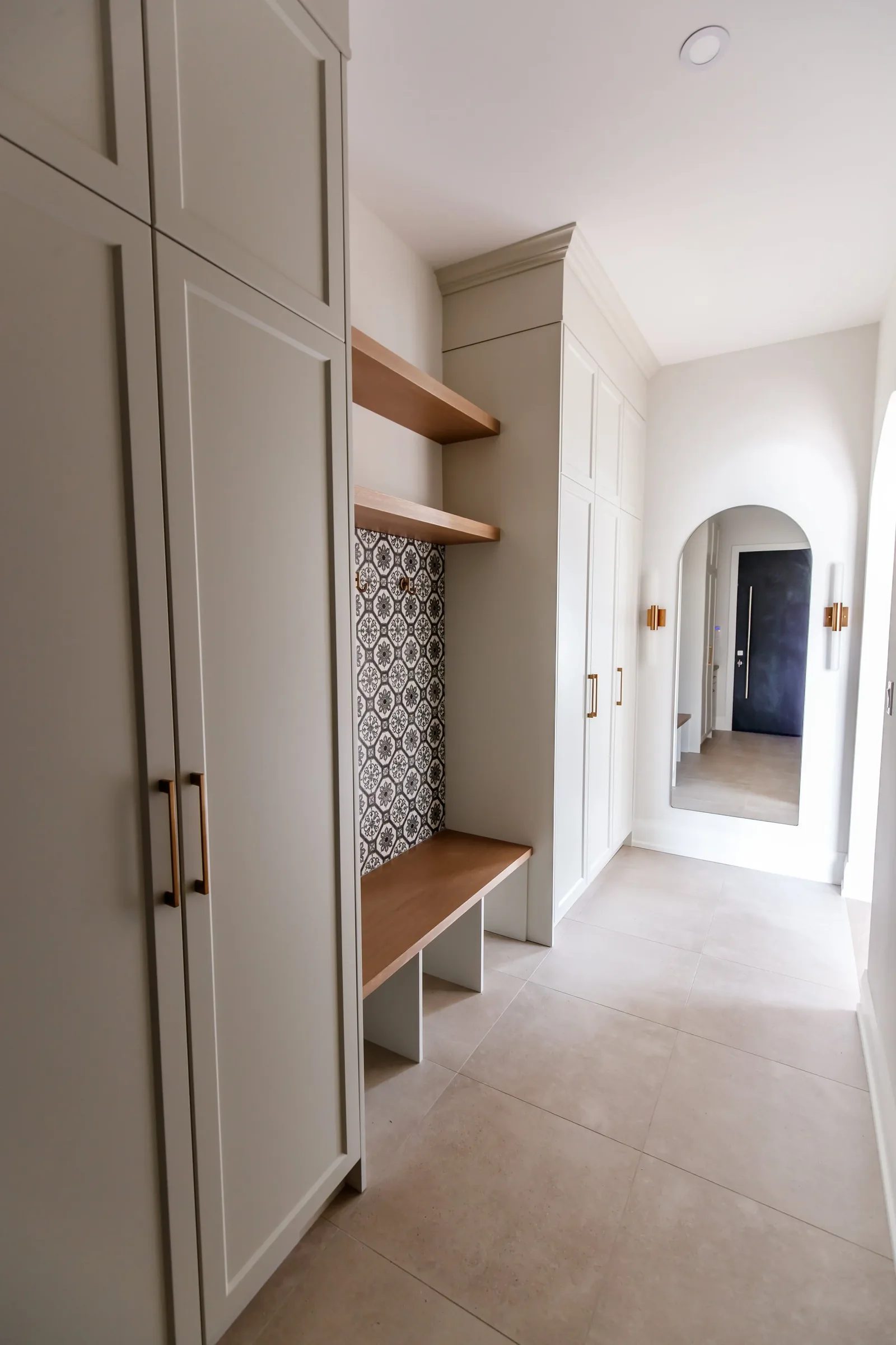 Mudroom with oak bench and patterned tile niche leading through an arched hallway to a navy front door.