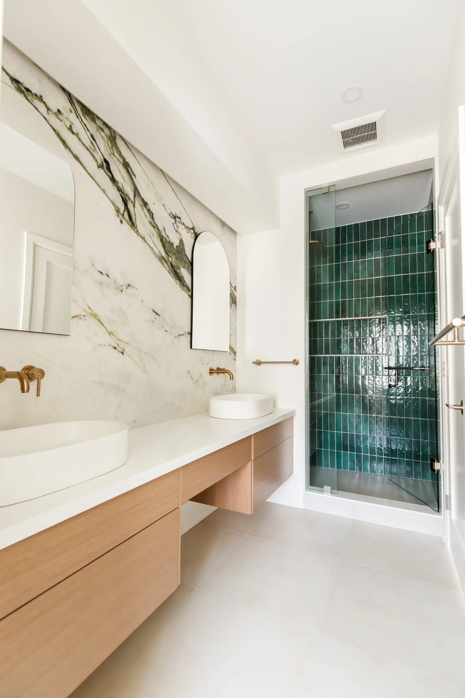 Primary bath with marble vanity wall and emerald tile shower behind clear glass.