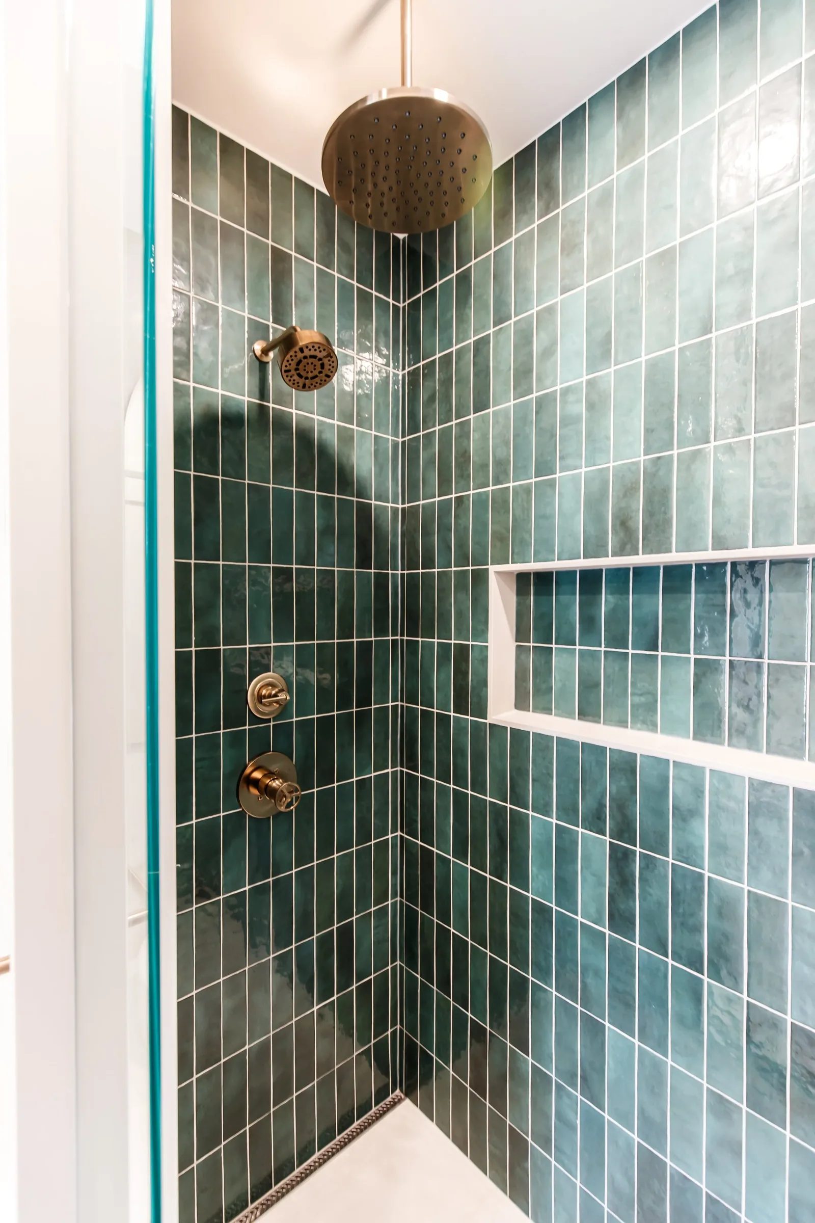 Emerald vertical tile shower with hammered brass rainfall head and recessed niche.