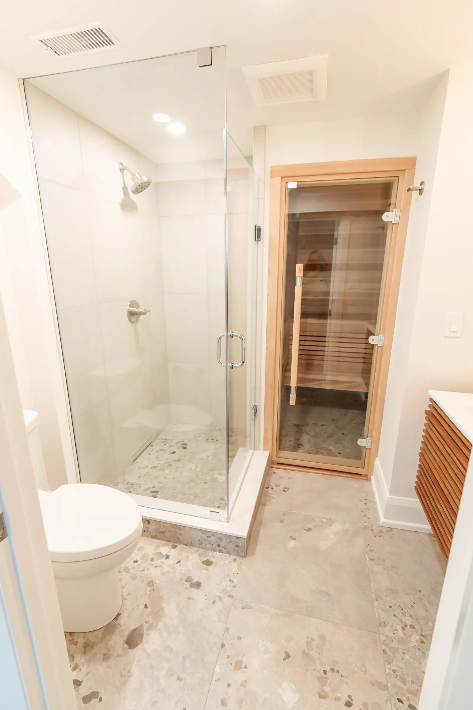 Spa bathroom with frameless glass shower, cedar sauna and terrazzo tile floor in a finished basement.