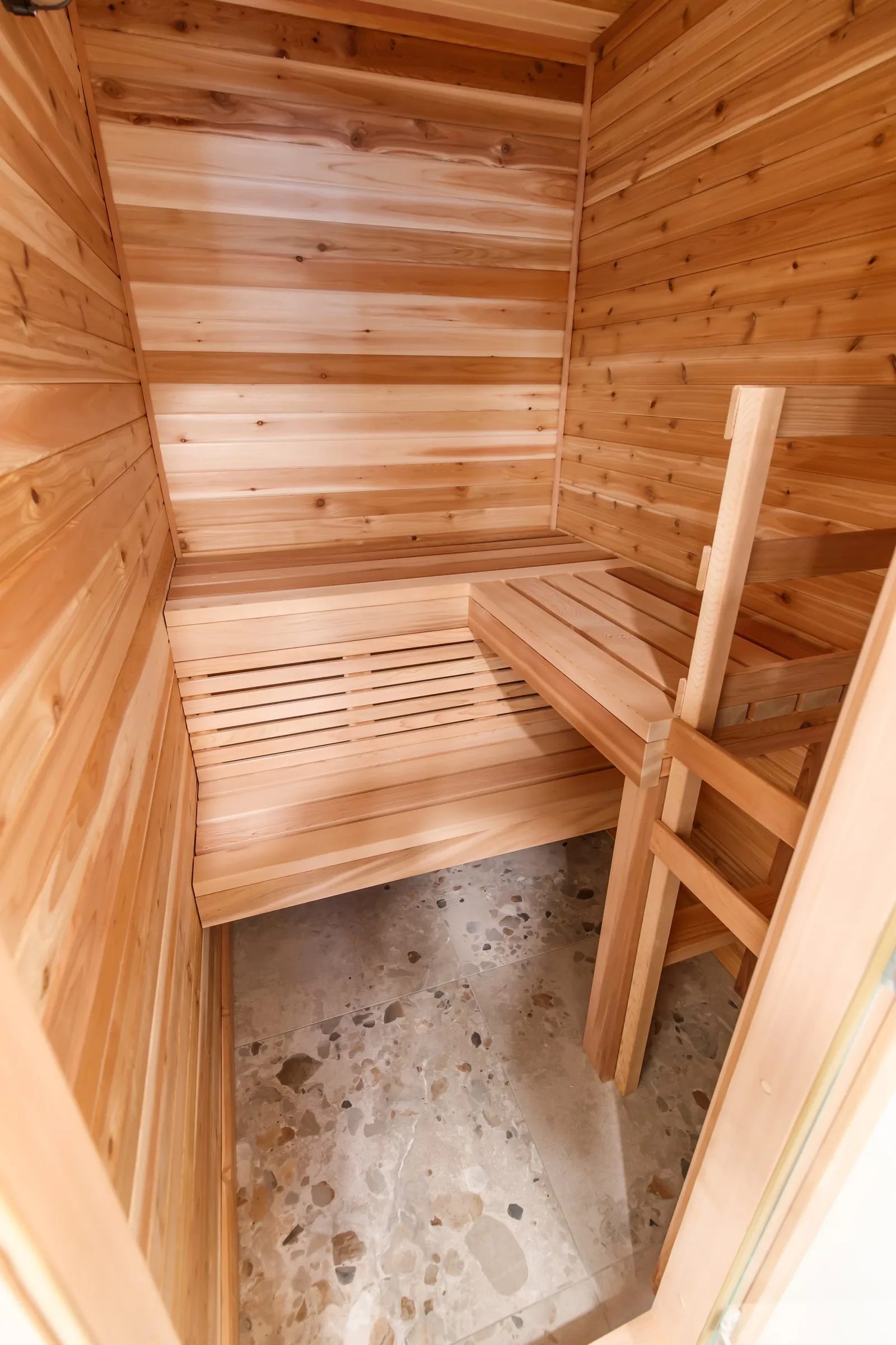 Interior of a cedar home sauna with tiered benches and a vertical cedar ladder over terrazzo tile.