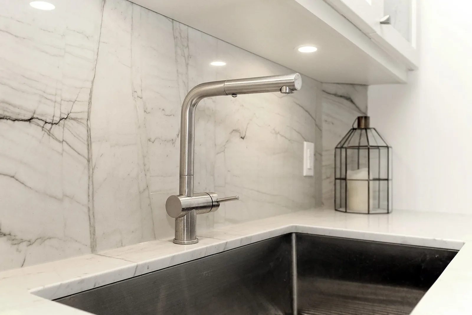 Contemporary kitchen detail featuring a sleek stainless steel faucet, undermount sink, and stunning white marble backsplash.