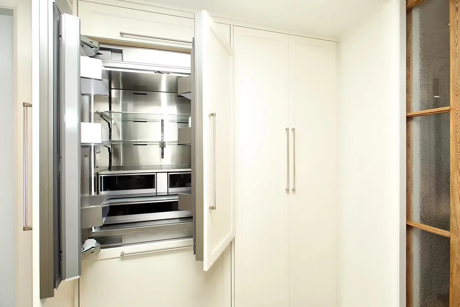 Warm white kitchen cabinetry frames a built in stainless refrigerator with long brushed metal pulls.