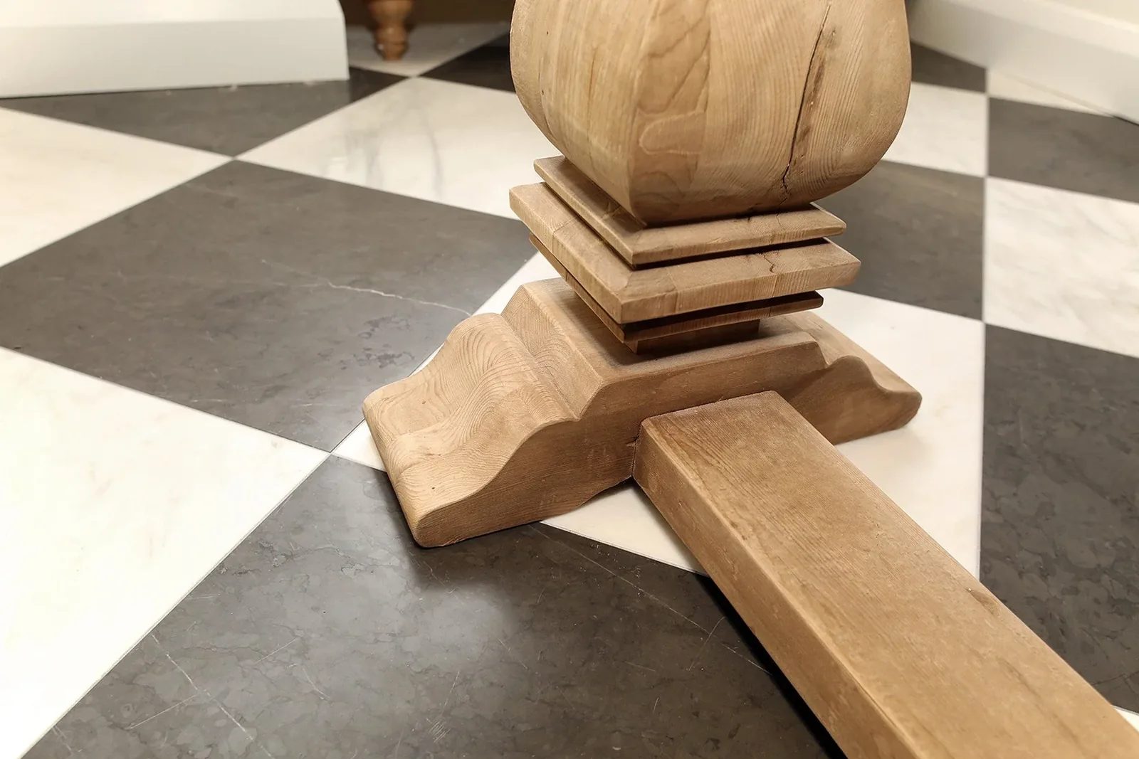 Carved oak table base on a black and white checkerboard tile floor, shown as a finished interior detail.