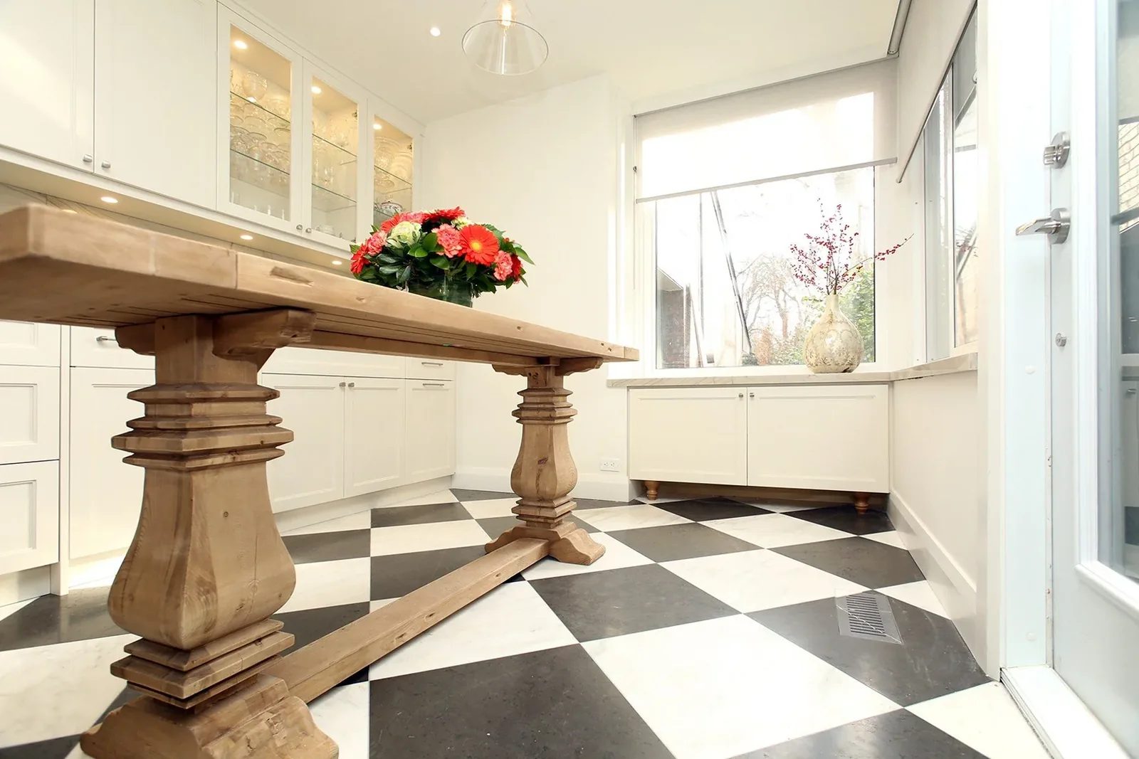 Renovated Toronto kitchen featuring white shaker cabinets, a large wooden dining table, and a black and white checkerboard.