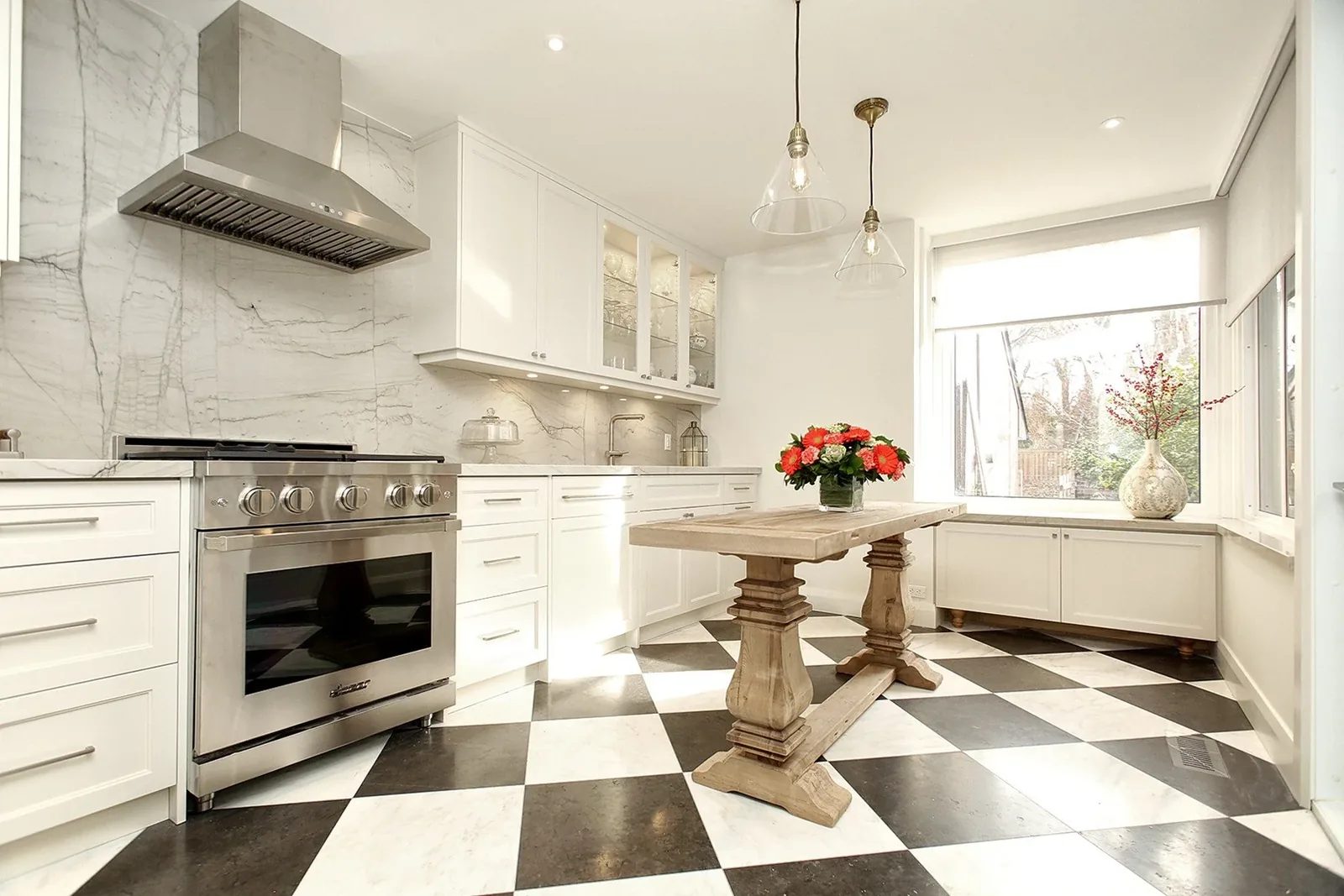 Bright white kitchen renovation with marble walls, checkered floor, wood island, and large window seating.