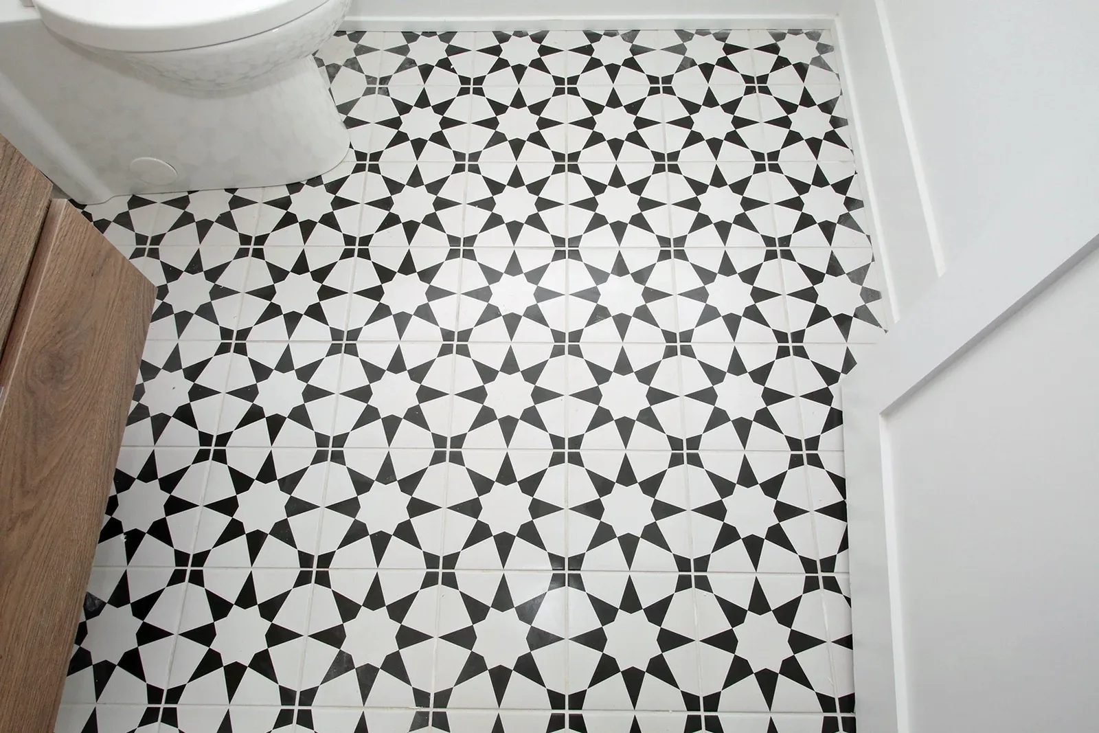 Black and white geometric tile adds contrast beside a white toilet and natural wood vanity.