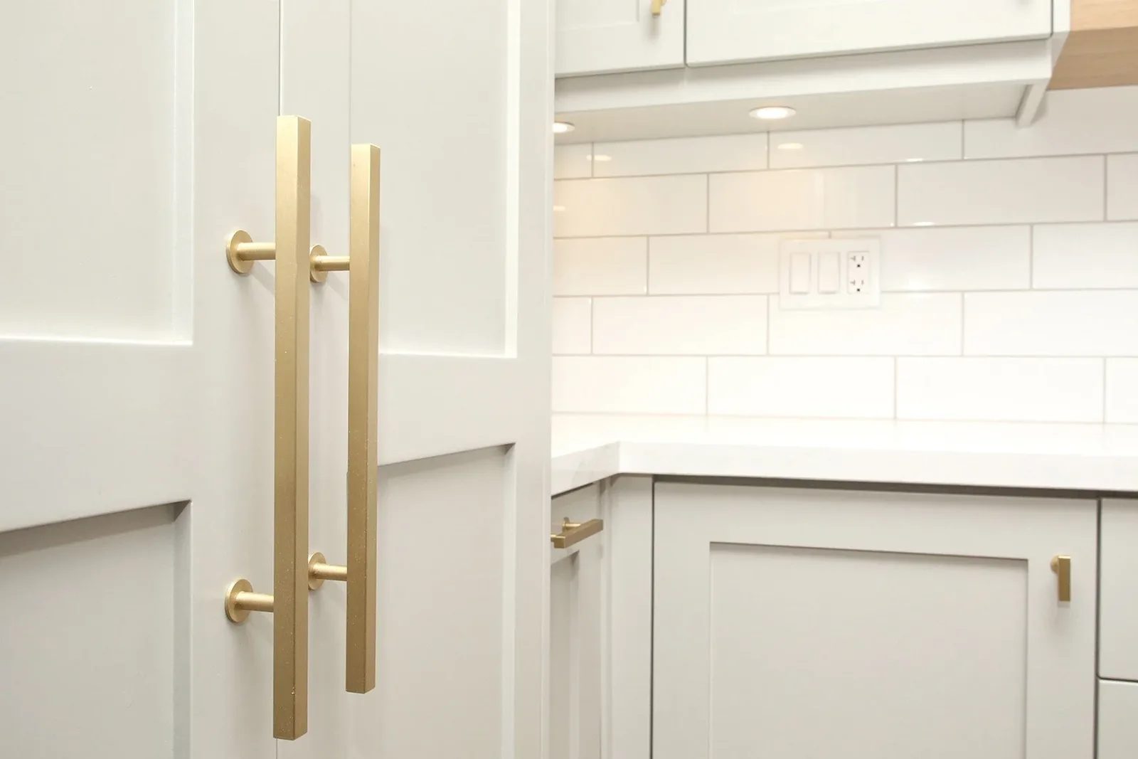 Warm white kitchen cabinetry with brushed brass pulls, quartz counters, and glossy subway tile.