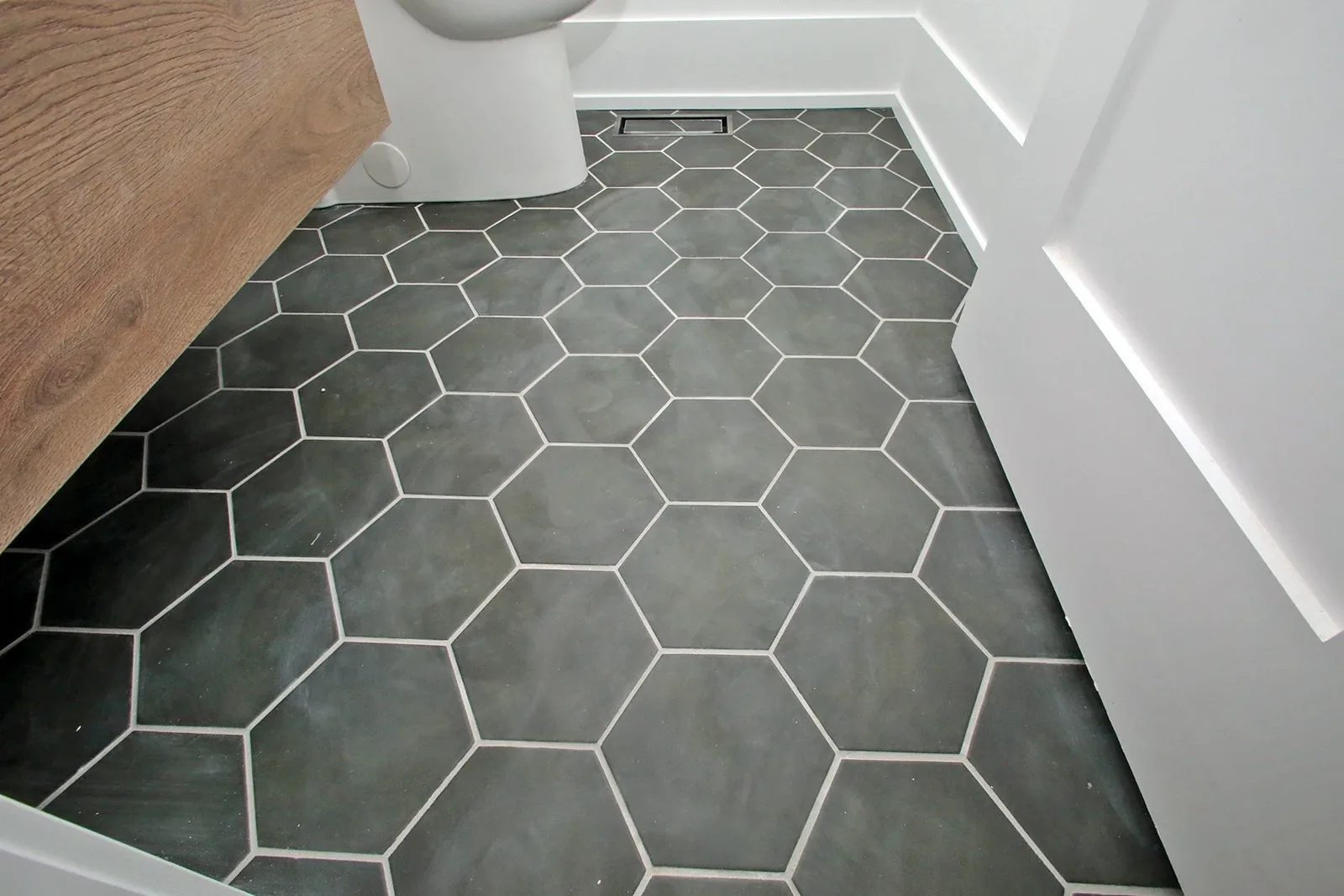 Charcoal hex tile floor with crisp white grout and a natural oak vanity in a modern bathroom.