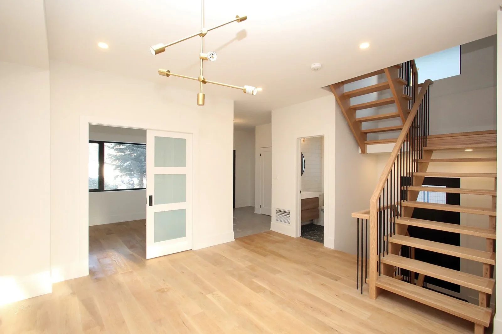 Finished open living area with natural oak stairs, warm white walls, and frosted glass sliding doors.