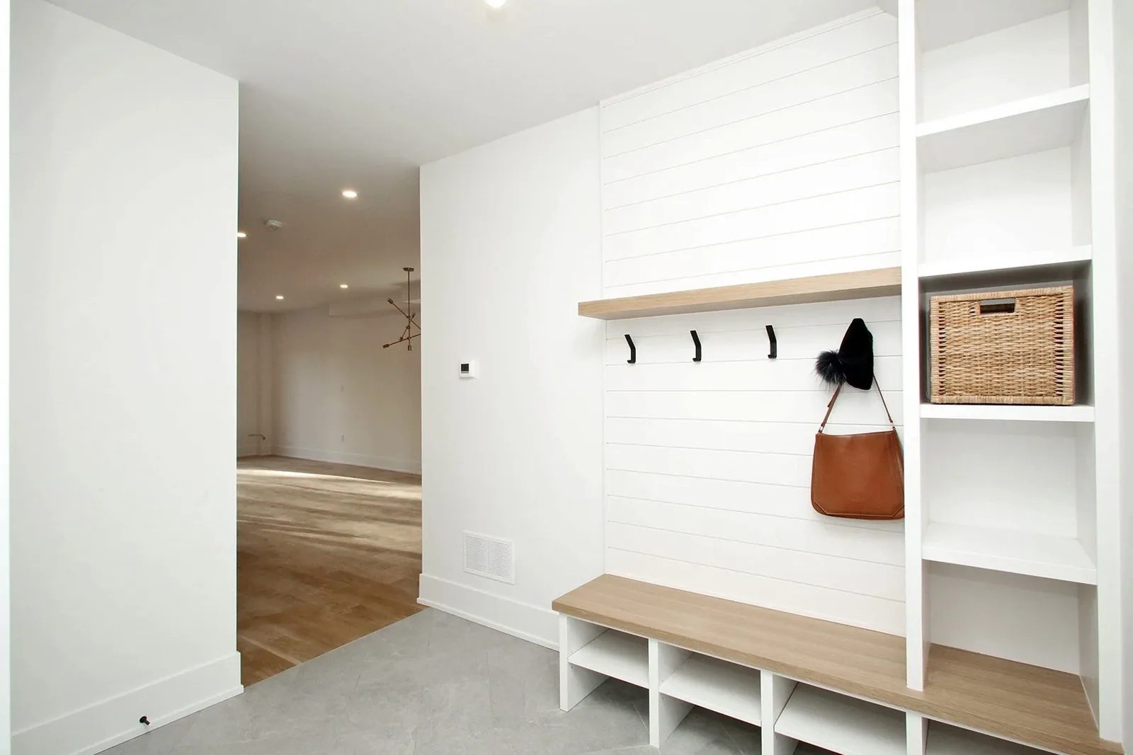 Bright entry with white shiplap, oak bench, black hooks, cubbies, and grey tile flooring.