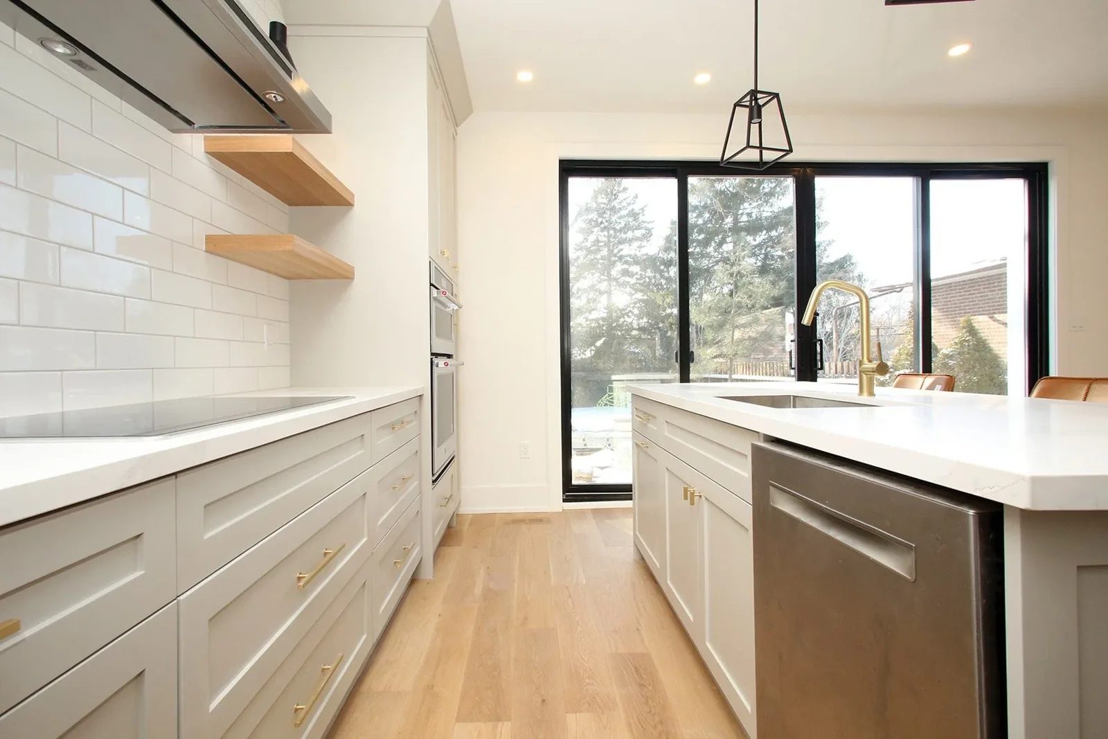 Bright Toronto kitchen with warm white shaker cabinets, oak floors, brass hardware and a large quartz island.