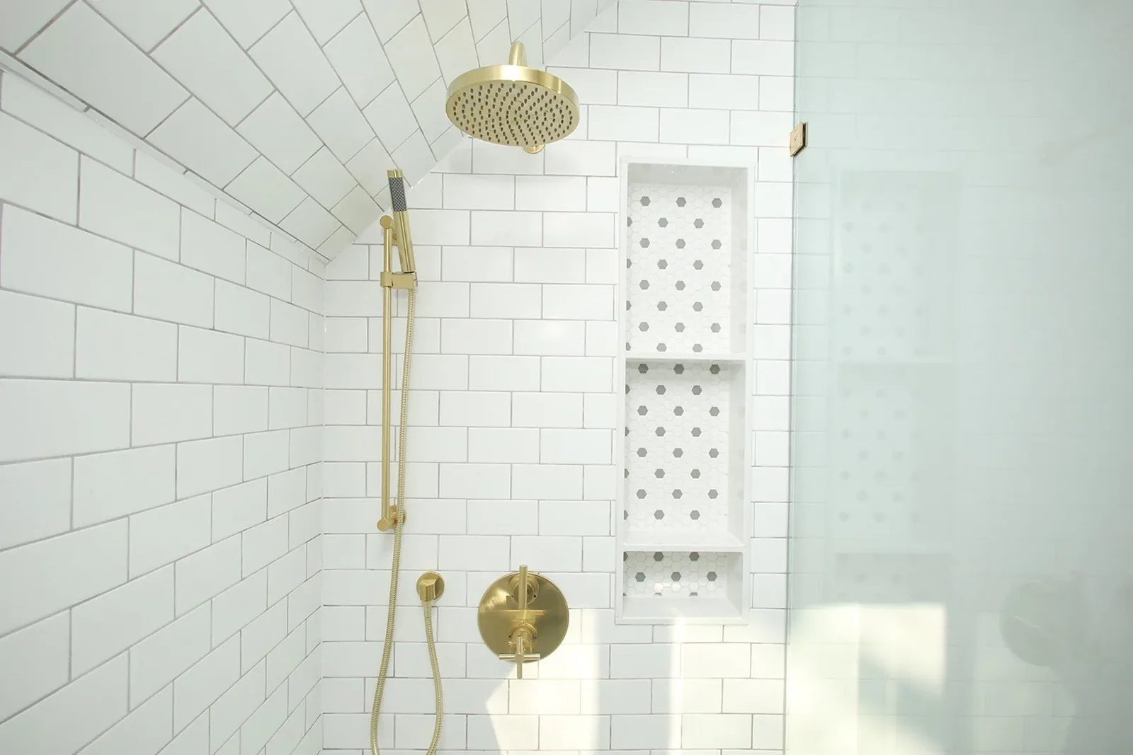 Bright white tiled shower with brushed brass fixtures, a glass panel, and a recessed niche.