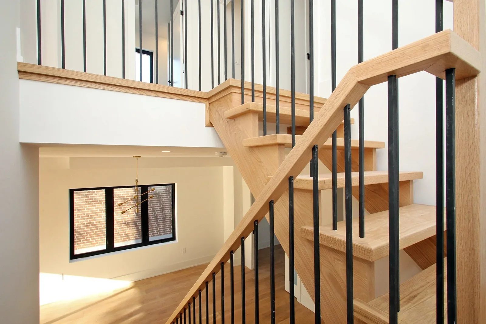 Natural oak staircase with black metal railings above a bright open living area.
