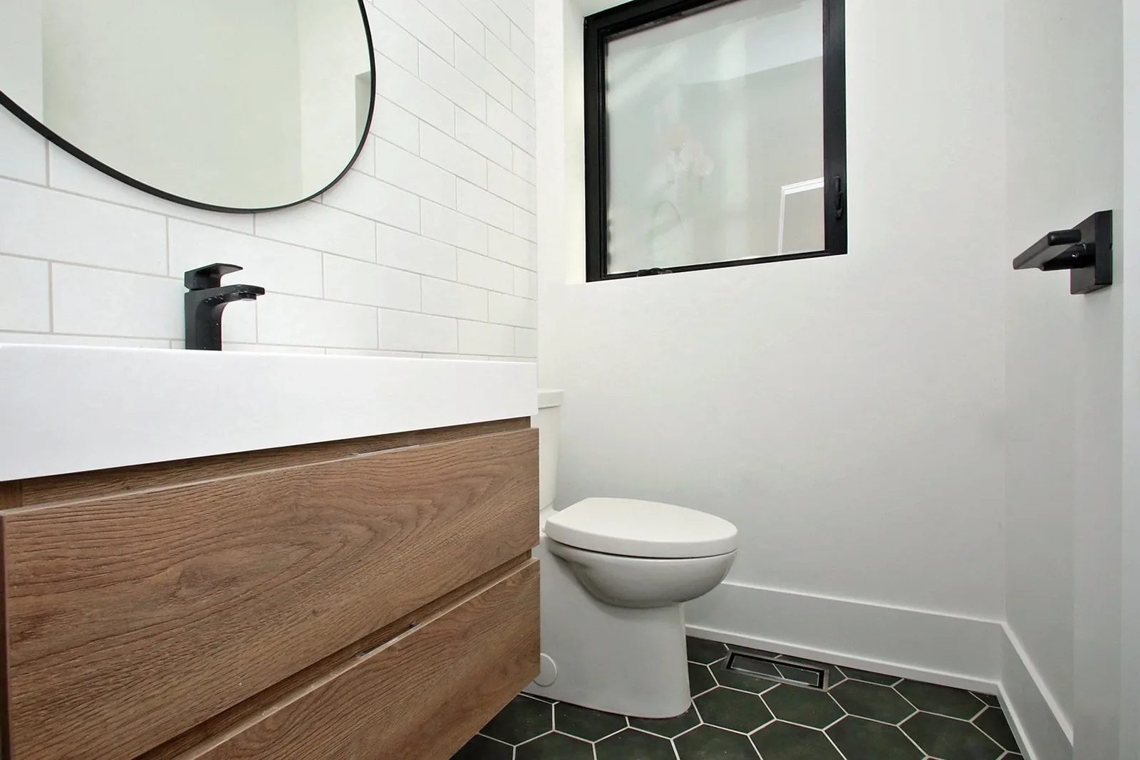 Finished bathroom with oak vanity, black fixtures, white tile, and dark hex floor for a Toronto renovation.