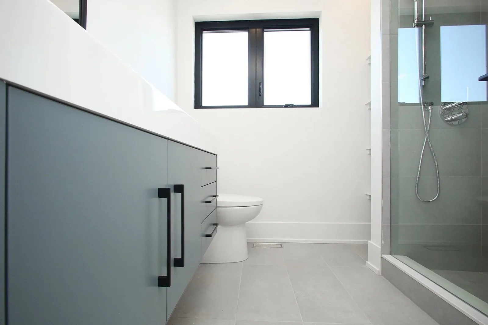 Modern white and grey bathroom with a vanity, toilet, window, and glass shower enclosure.