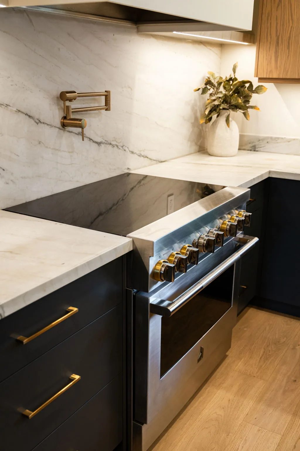Stainless pro range against a marble slab backsplash with navy cabinetry and brass pulls.