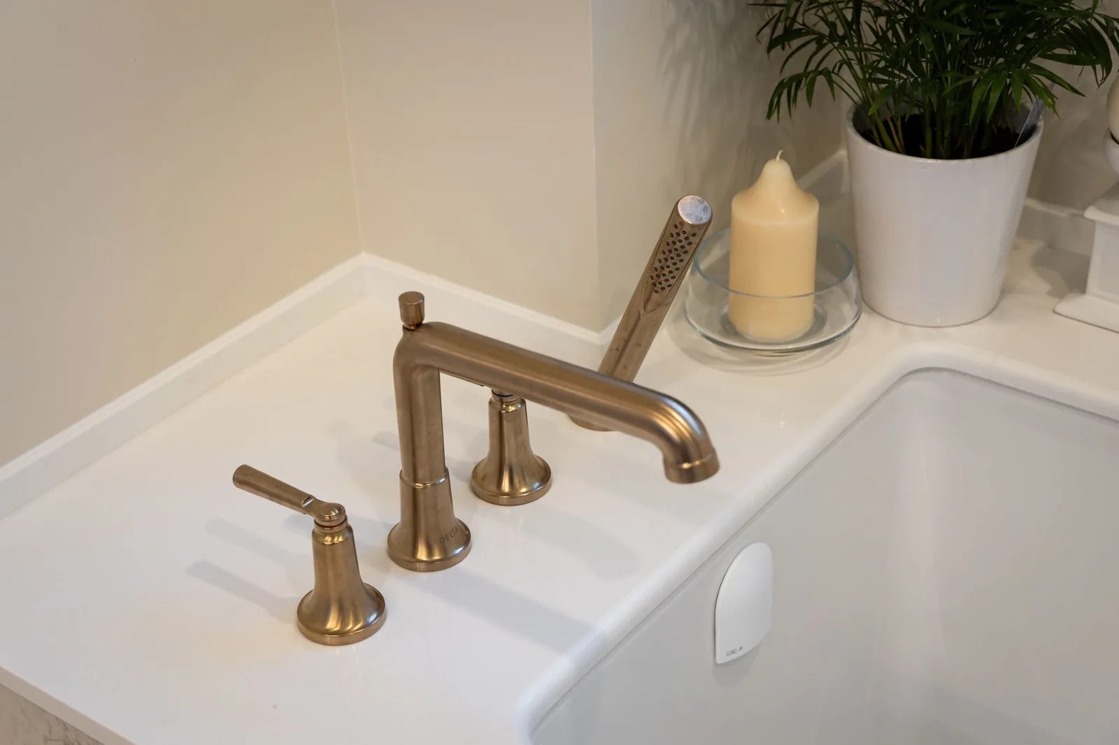 Freestanding tub detail with a floor-mounted brass filler, a potted plant, and a candle on the tub deck.