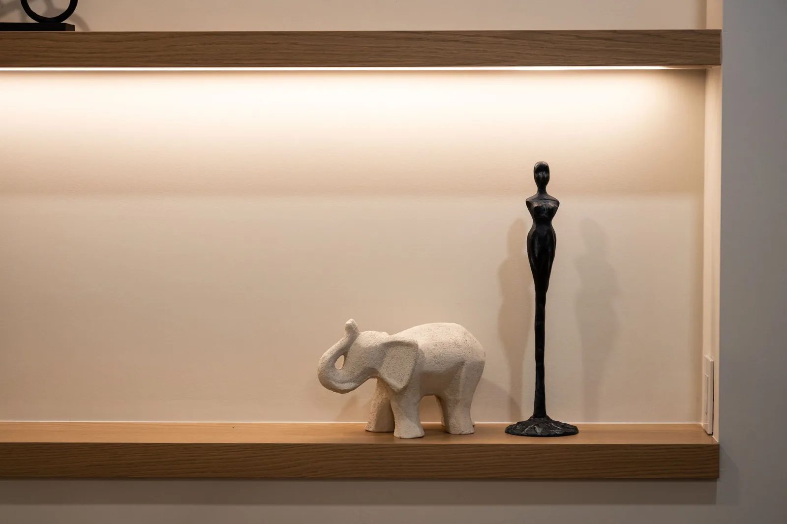 Lit built-in niche with floating oak shelves styled with a figurine and a small sculpture.