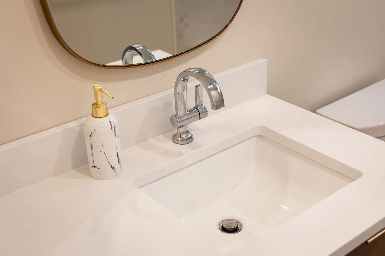 White undermount sink with a brass faucet on a marble vanity top.