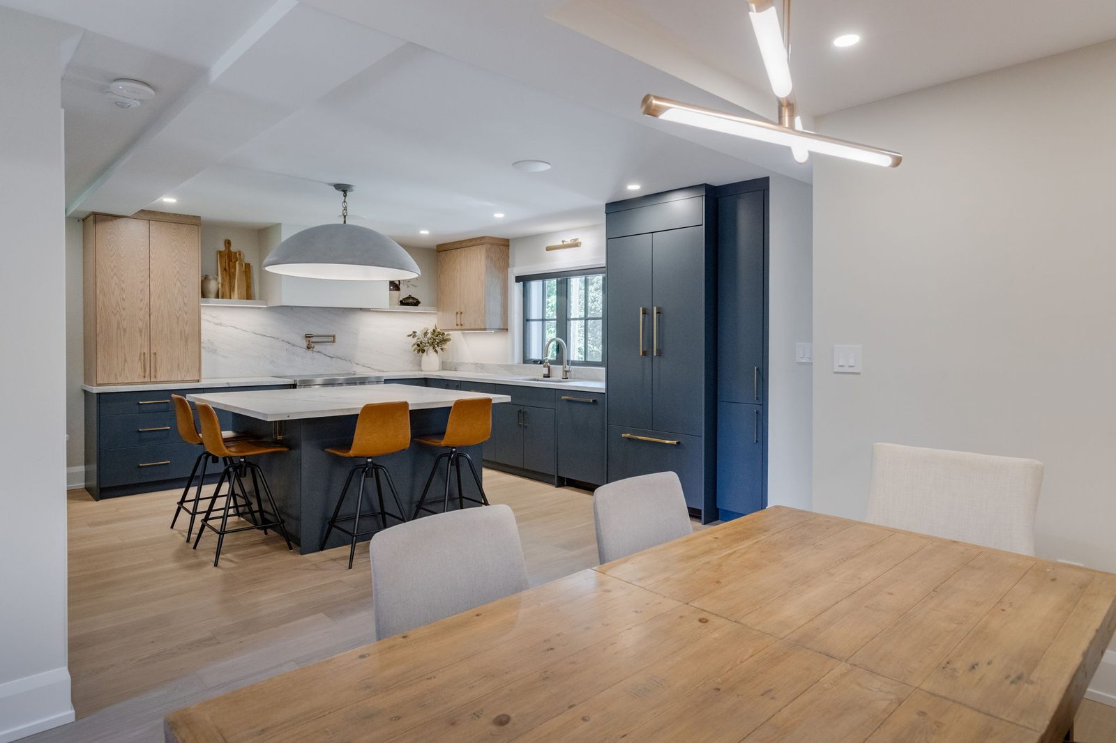 Kitchen seen from the dining side, with a linear pendant overhead, the navy island and the panelled full-height cabinet run.