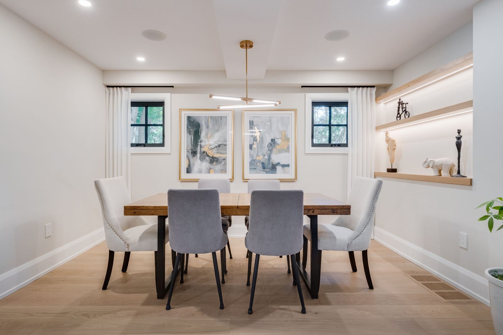 Dining room with a recessed ceiling detail, a lit white oak display niche on the far wall and black casement windows.