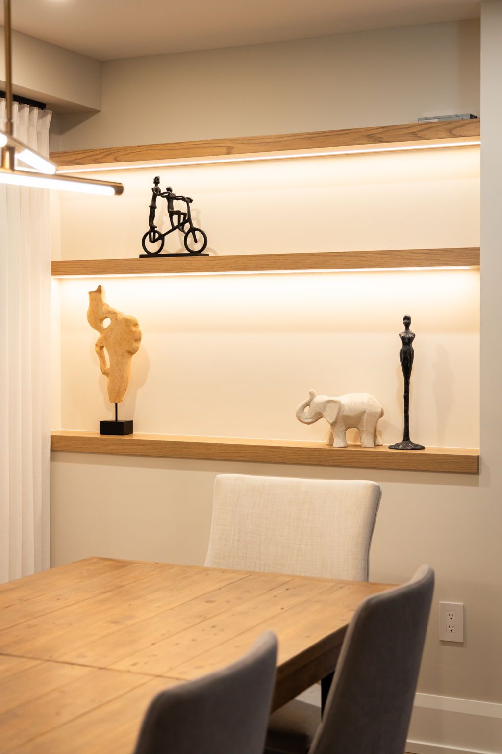 Lit white oak display shelves recessed into the dining room wall, with integrated lighting washing each shelf.