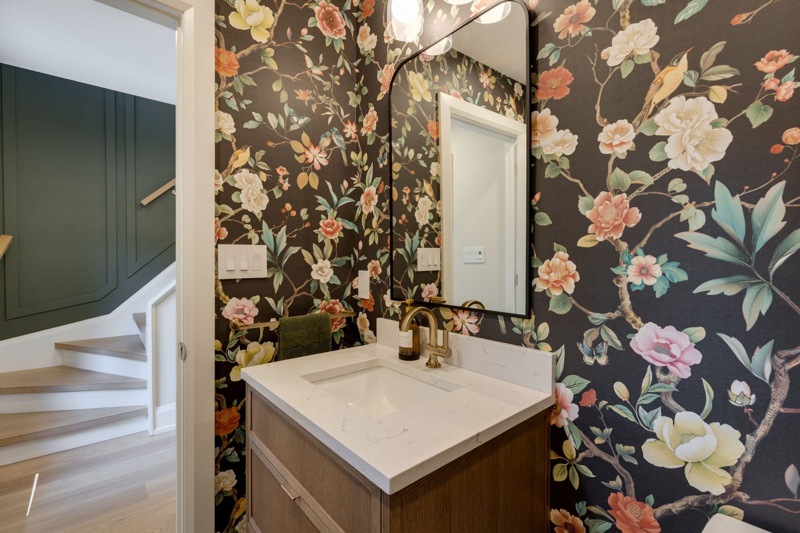 Powder room seen from the stair side, so the deep green panelled staircase and the walnut vanity read in one frame.