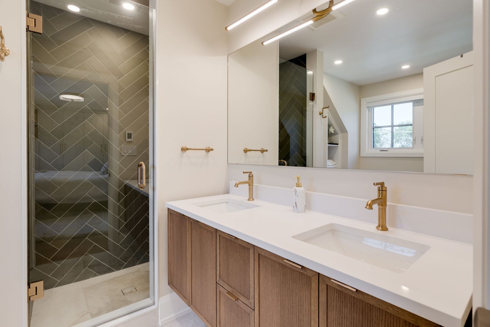 Main bathroom with a reeded walnut double vanity, a stone counter with an integrated backsplash, brass tapware and a frameless glass shower in green herringbone tile.