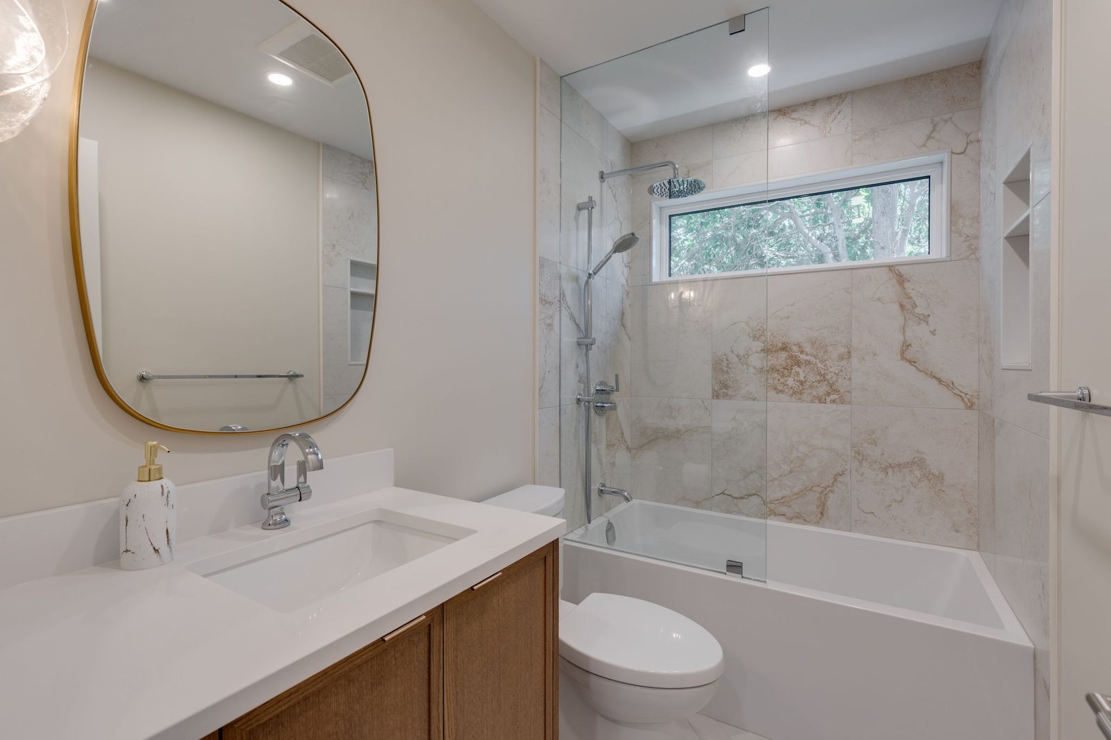 Second bathroom with an oak vanity, a stone counter, a tub set into a stone-clad alcove and a recessed niche under a transom window.