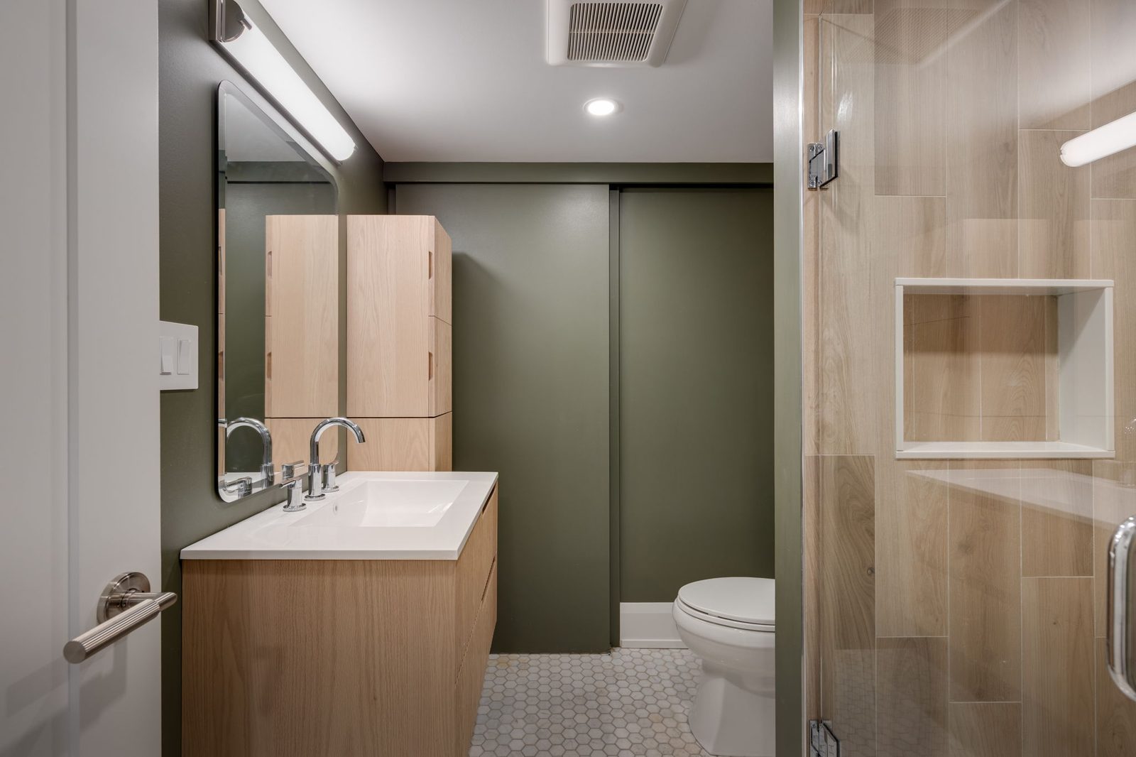 Ensuite with a deep green feature wall, a floating fluted walnut vanity, a frameless glass shower enclosure and a hex tile floor.