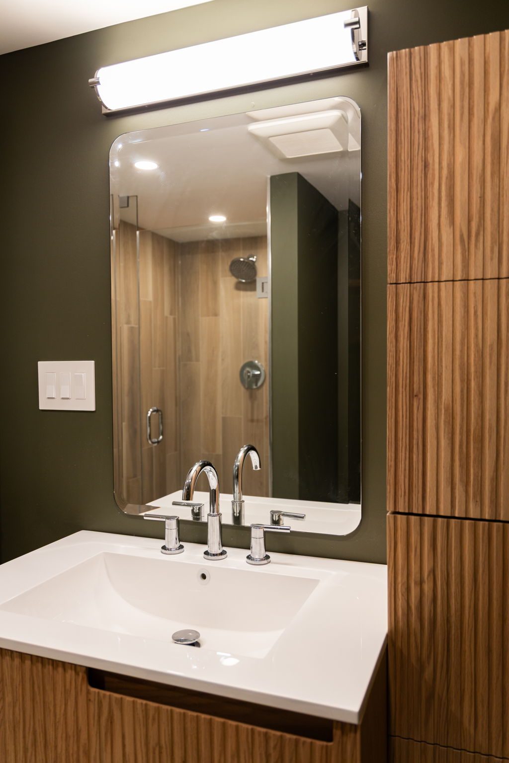 Fluted walnut ensuite vanity with a frameless mirror and the tiled shower reflected behind it.