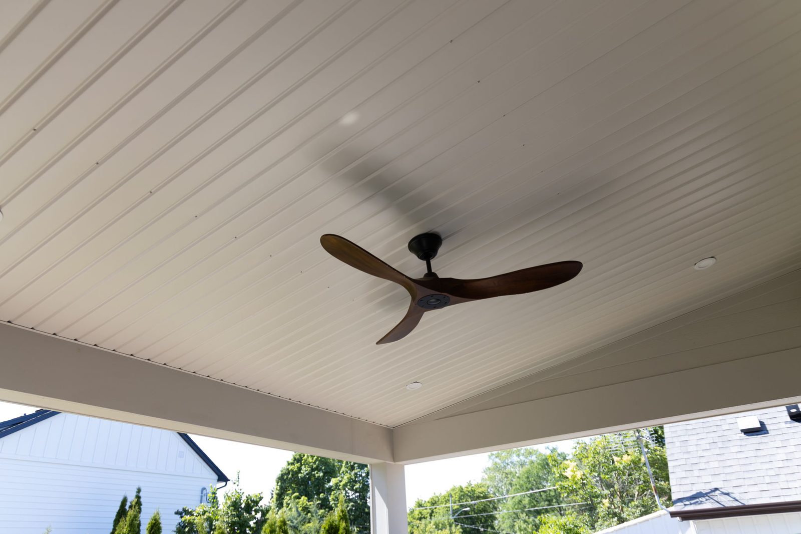 Painted tongue-and-groove porch soffit seen from below, with a dark-bladed ceiling fan at its centre.