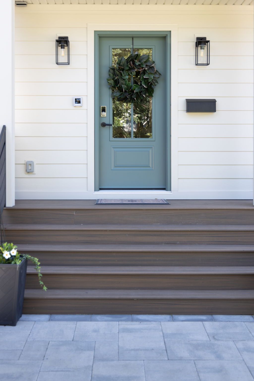 Front entry in detail, with a soft teal painted door, black lantern sconces, white shiplap siding and wide timber steps.