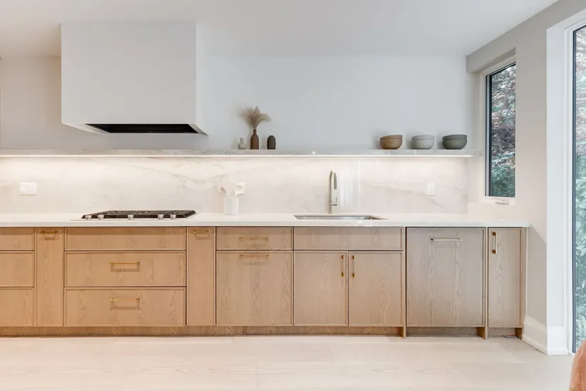 Quiet Oasis: white oak kitchen run with a stone slab backsplash, floating shelf, gas cooktop, and an integrated hood, by Waterfront Home Improvements