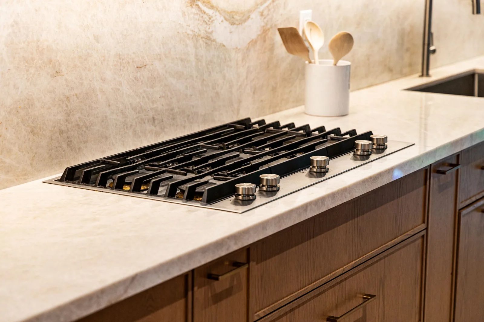 Black gas cooktop set into a marble counter with white oak cabinetry below.