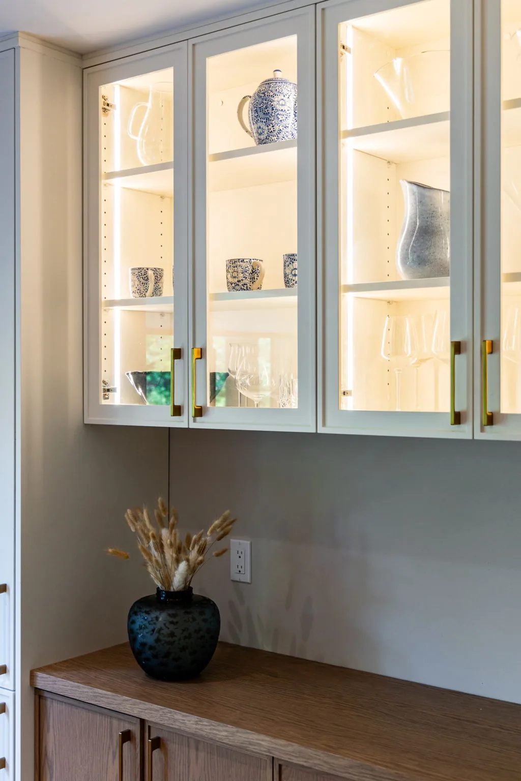 Glass-front upper cabinet with interior lighting displaying dishware and glassware.