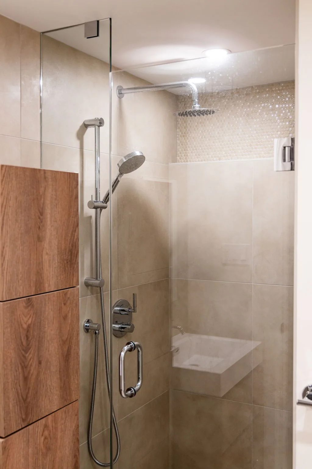 Walk-in shower with a rainfall head, a handheld sprayer, and a built-in bench in wood-look and marble tile.