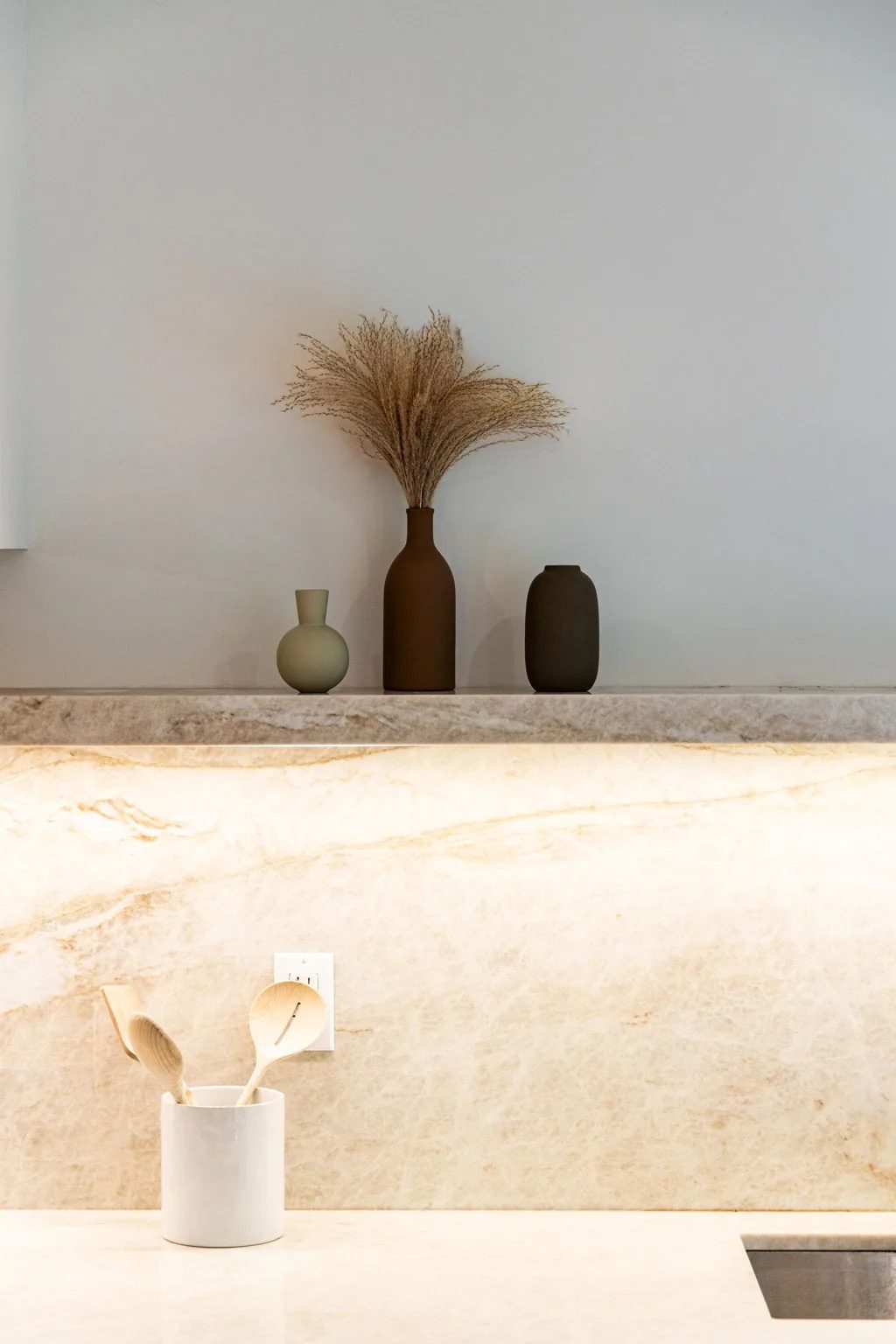 Marble counter and backsplash styled with ceramic vases beside white oak cabinetry.