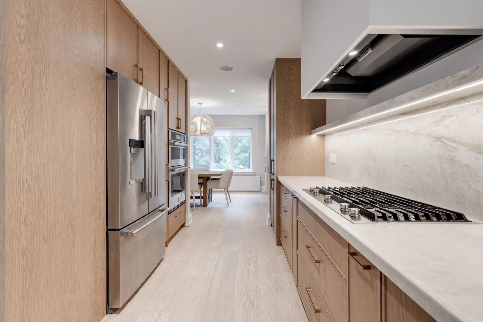 Galley kitchen in white oak with a stainless french-door refrigerator, stone counters, and a gas cooktop.