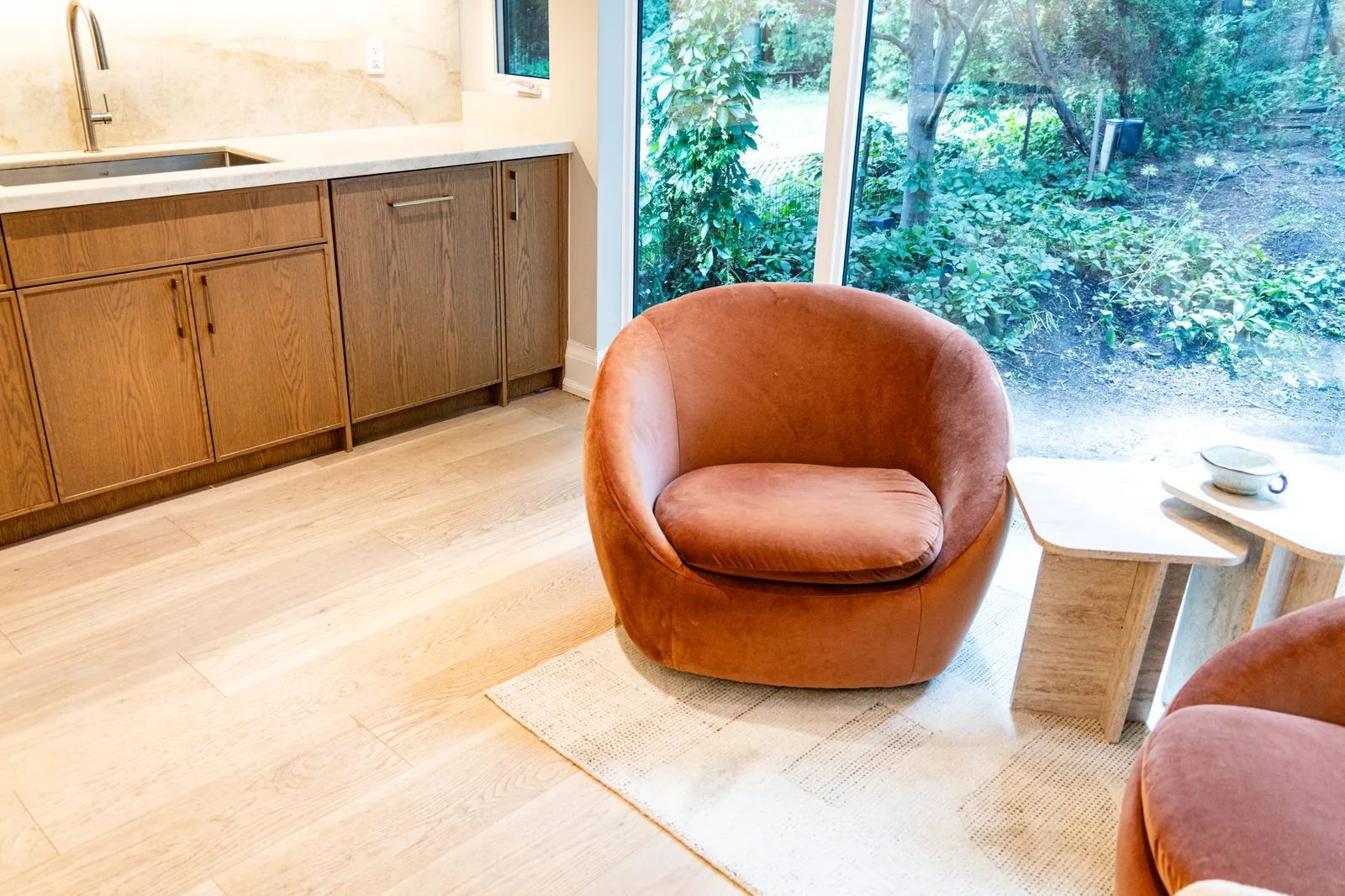 Kitchen with white oak cabinetry and an orange leather swivel chair set against floor-to-ceiling windows onto the ravine.