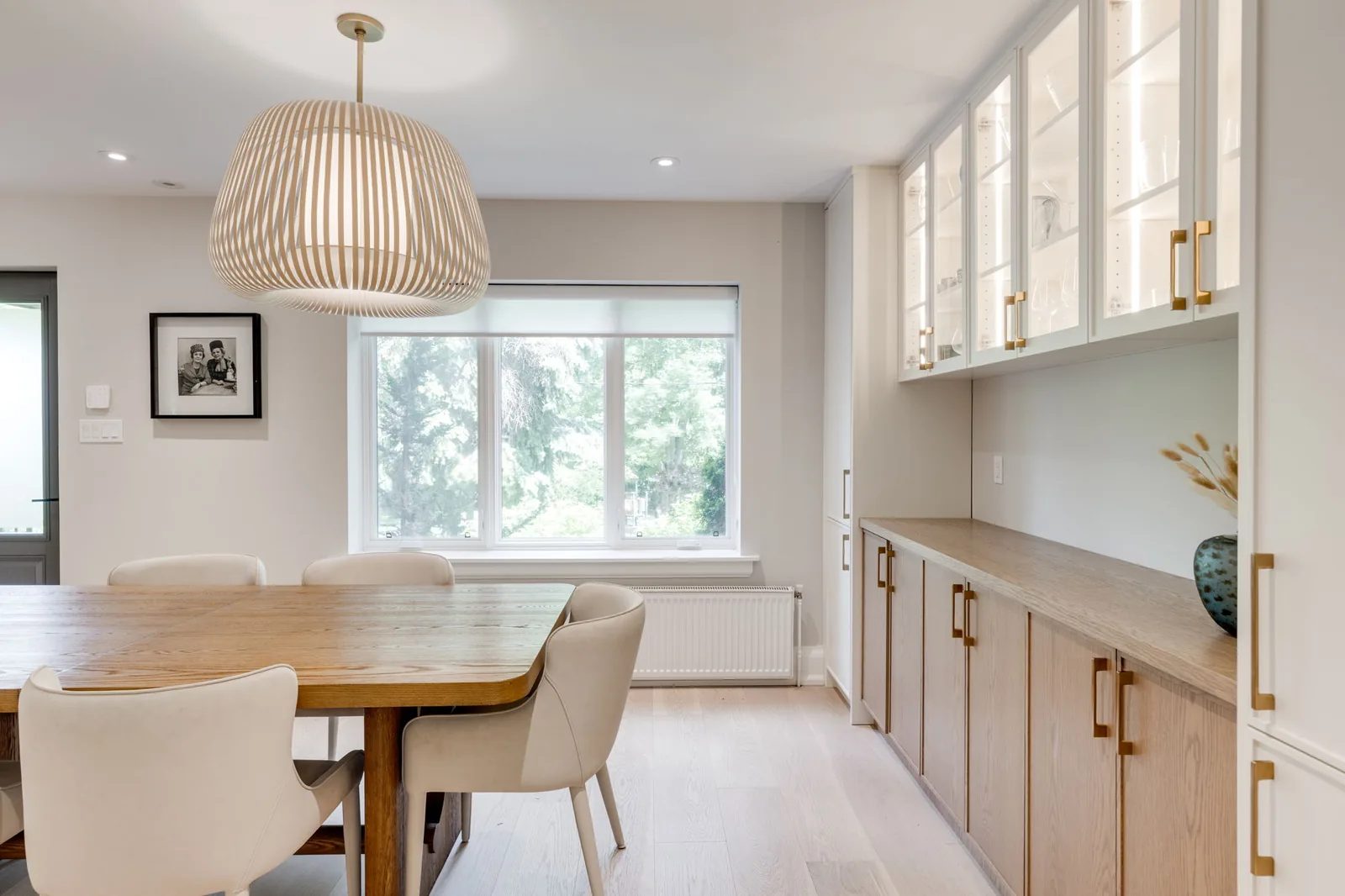 Dining and servery area with glass-front upper cabinets, a wood table, and a sculptural pendant.