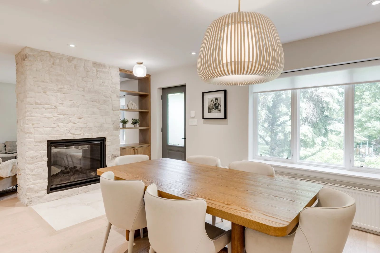Dining room with a wood table and white upholstered chairs beside a natural stone fireplace with integrated oak shelving.