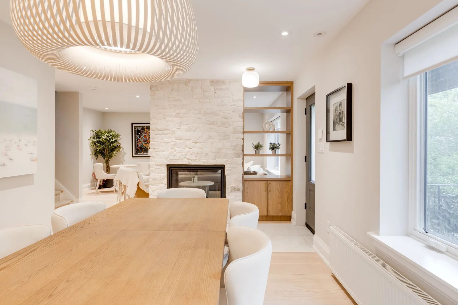 Dining area anchored by a natural stone fireplace with integrated shelving, a wood table, and white upholstered chairs.
