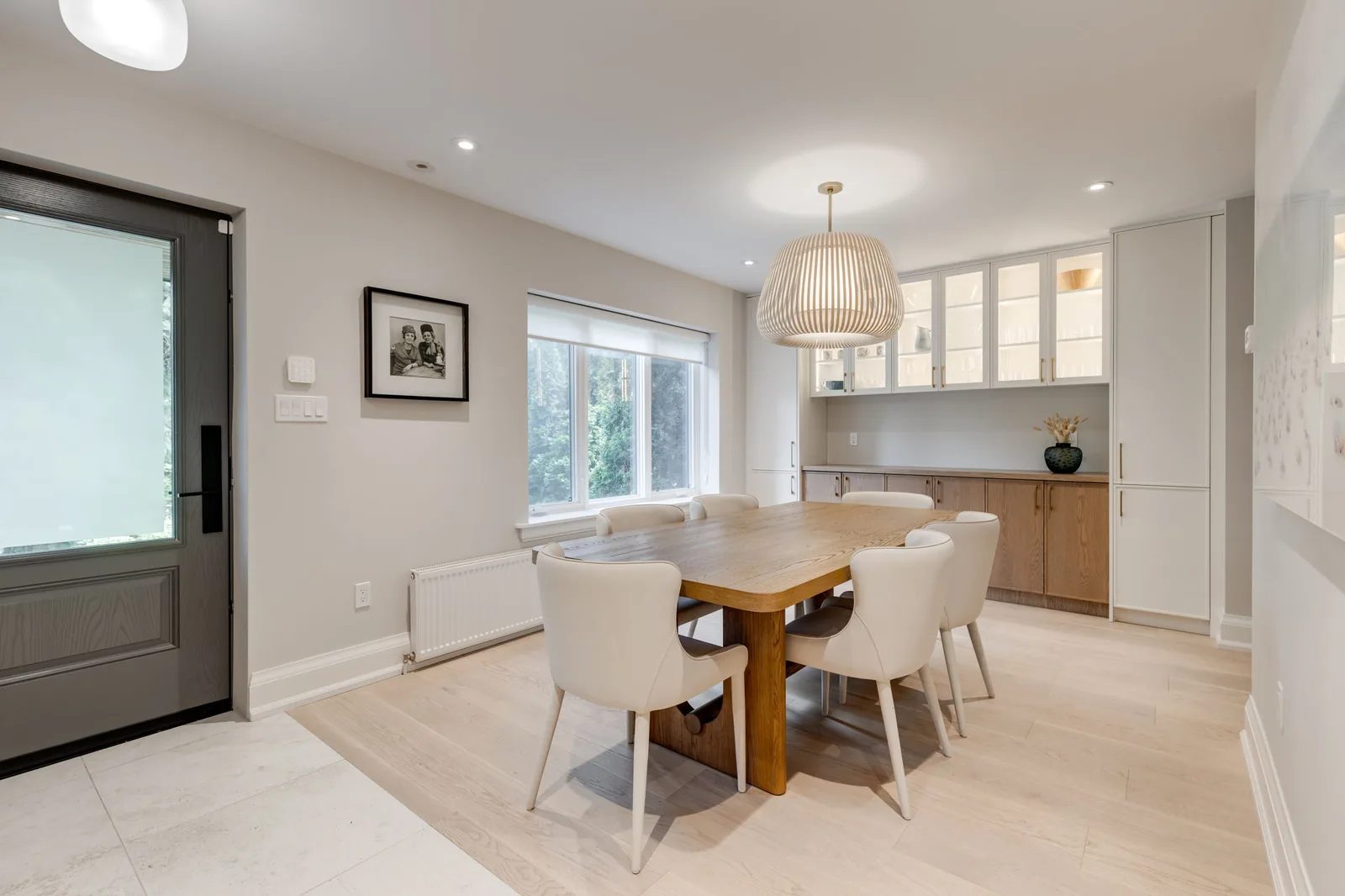 Dining room with a wood table, white upholstered chairs, a sculptural pendant, and a glass door to the garden.