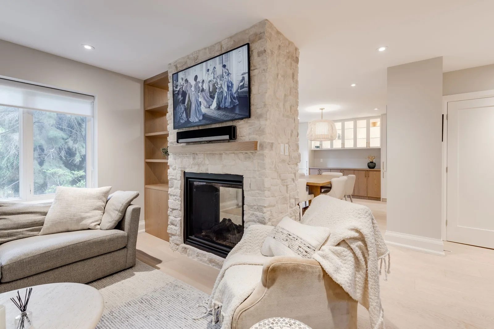 Living room with a sectional sofa facing a floor-to-ceiling natural stone fireplace with a wall-mounted television and oak shelving.