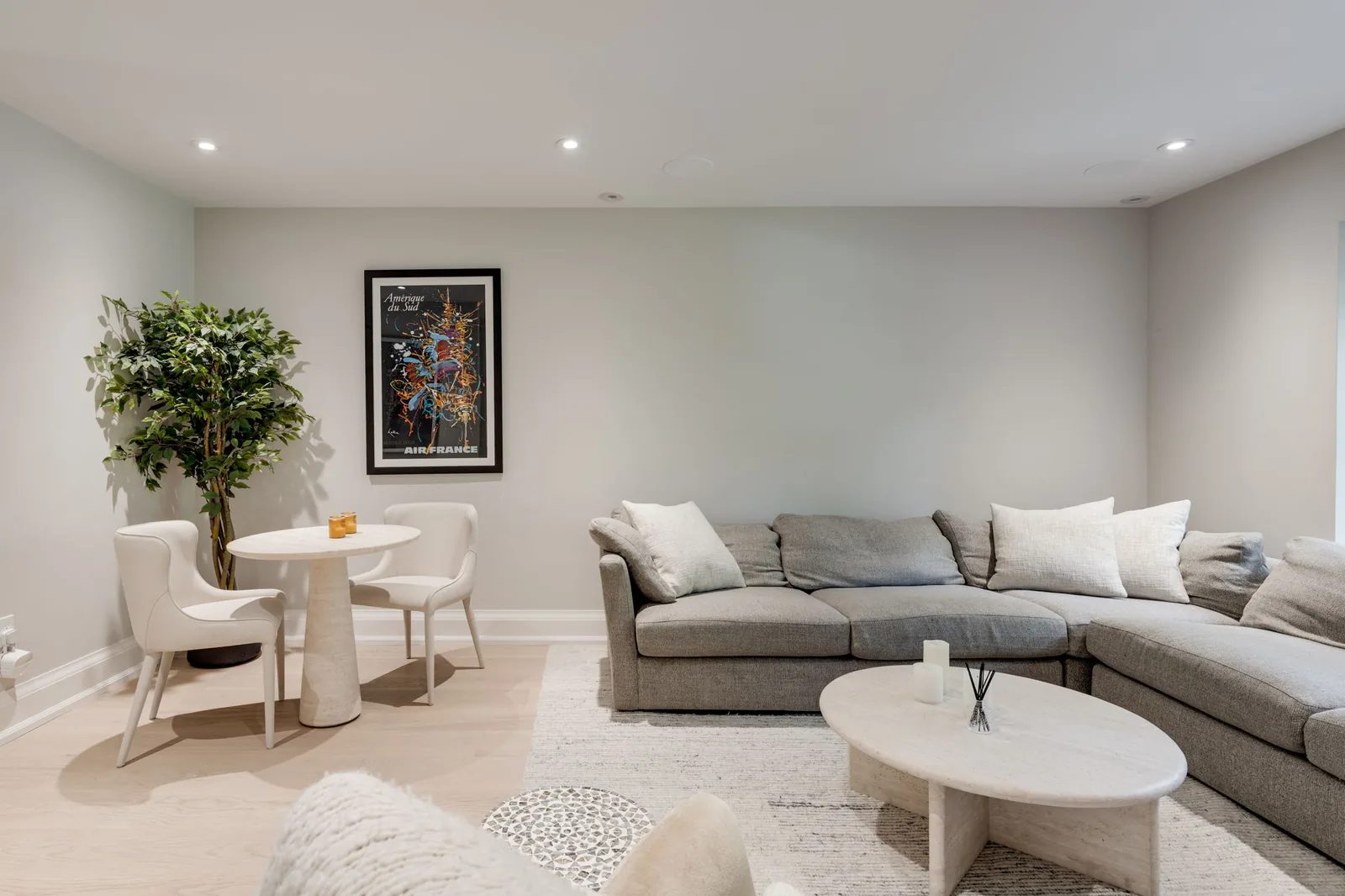 Living room with a sectional sofa, a compact dining nook, framed art, and a potted tree by the window.