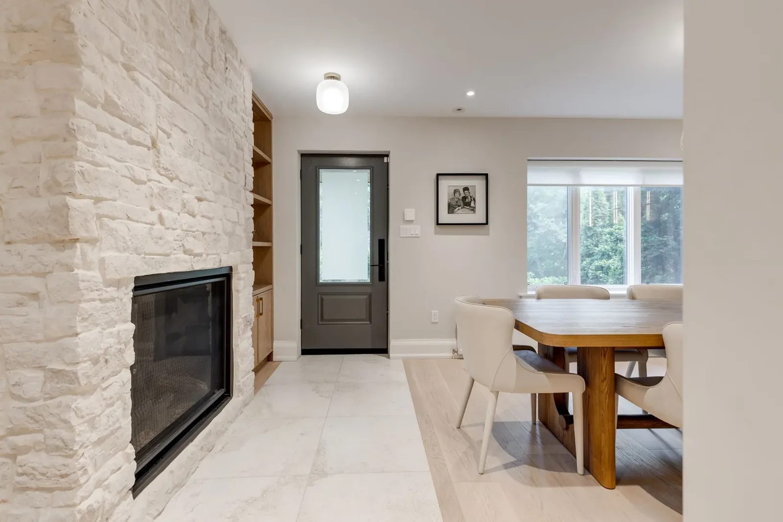 Dining area beside the whitewashed stone fireplace, with oak display shelving, a grey glass-panelled side door, and the table set by the window.
