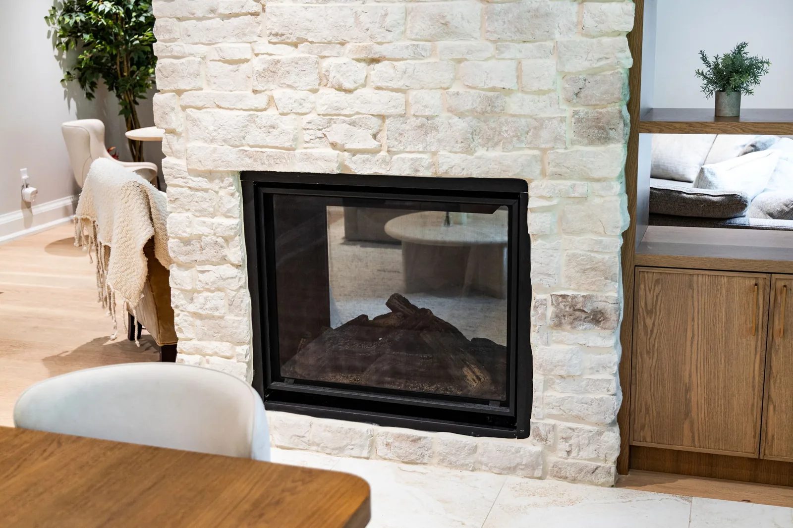 Great room with white upholstered chairs and a wood table set beside a floor-to-ceiling natural stone fireplace.