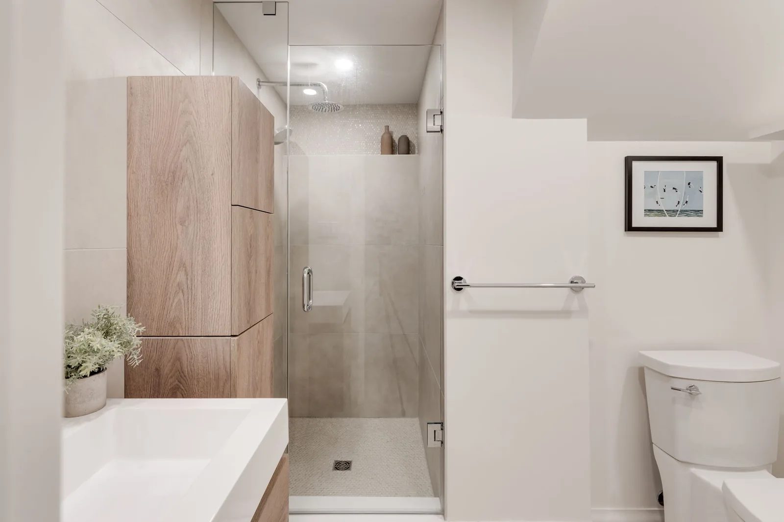 Bathroom with a frameless glass shower in large-format tile, a white oak storage tower, and a mosaic-tiled shower floor.